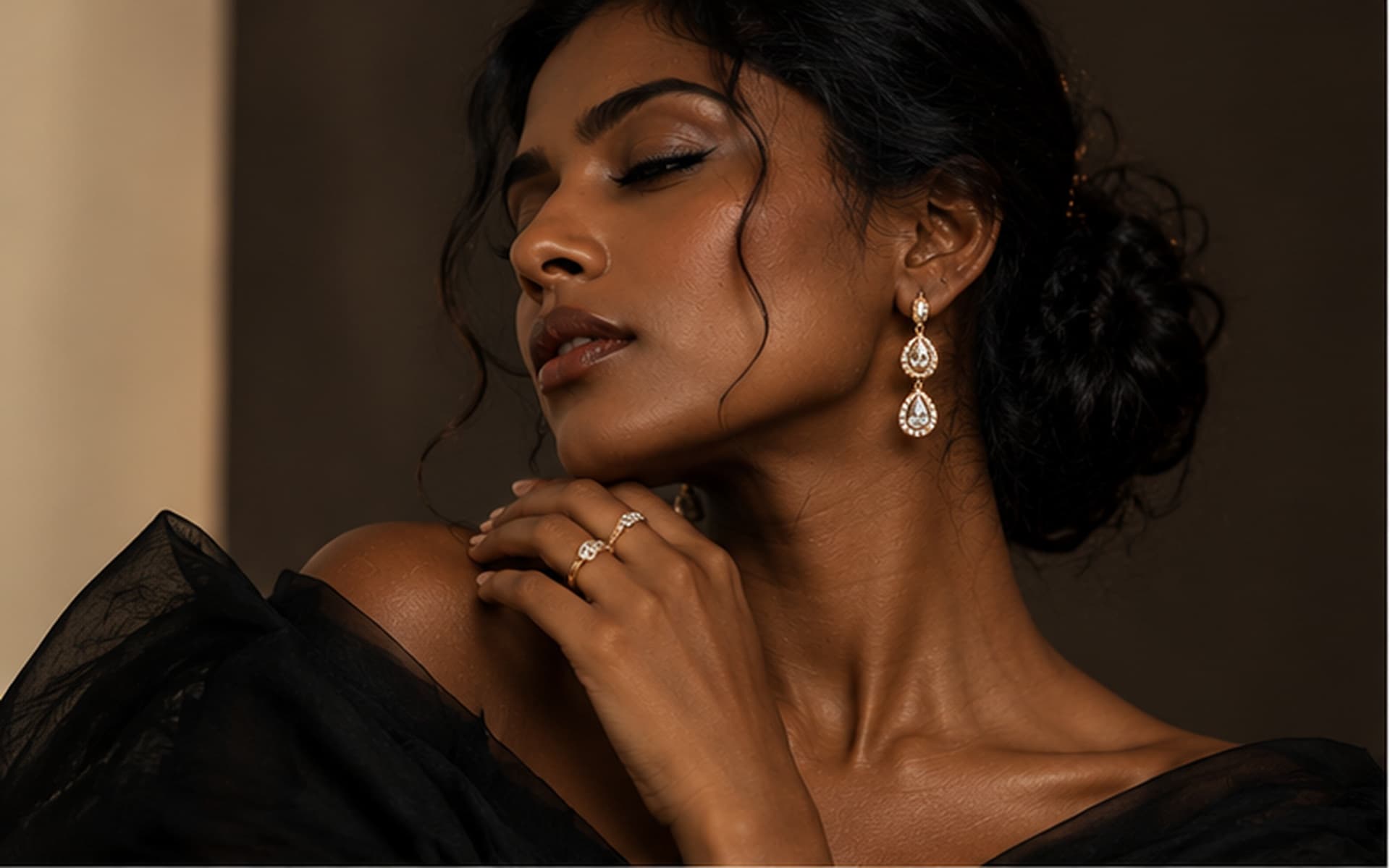 Smiling woman in a black top wearing a teardrop earring, gold watch and pendant necklace, warm daylight