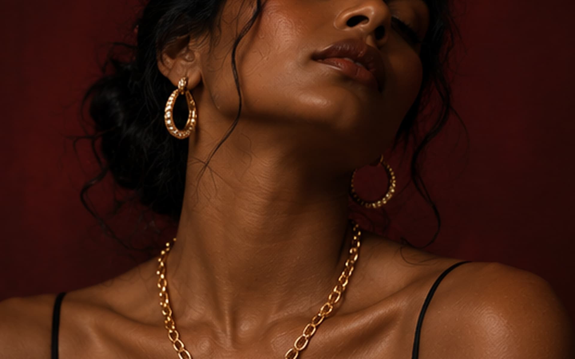 Woman in an emerald green dress wearing a coin necklace, bracelet and earrings, in front of green foliage