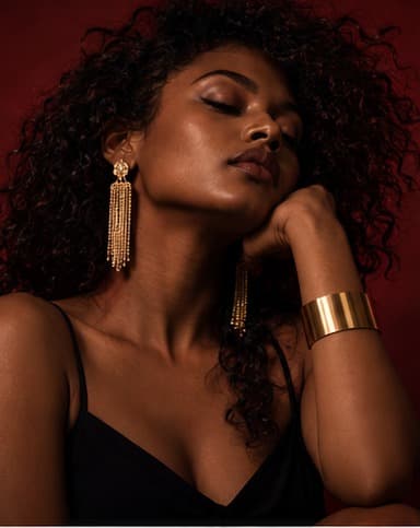 Woman with curly hair wearing fringe drop earrings and a gold cuff, moody red studio lighting