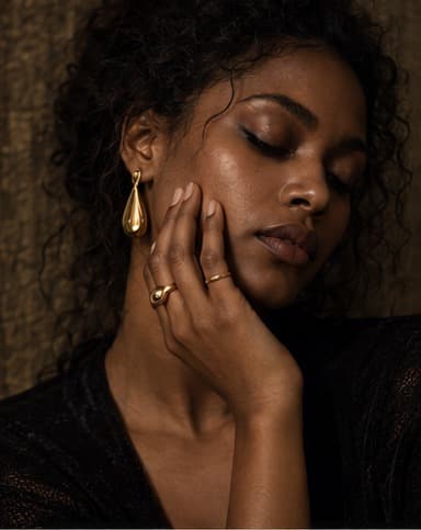 Close portrait of a woman wearing a teardrop earring and rings, hand resting against her face