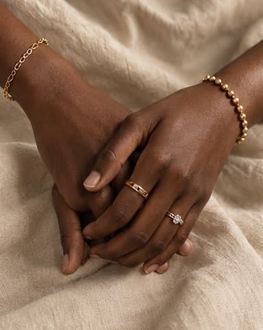 Two women's hands intertwined, wearing rings and layered chain bracelets