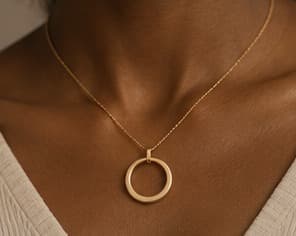 Gold necklace with a circular pendant, worn at the collarbone